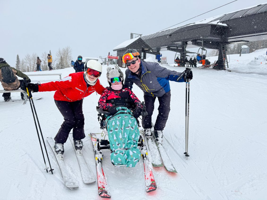 Tetra ski athlete posing for a photo on a snowing day, with her parents on either side.