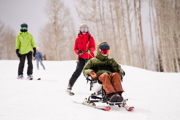Three skiers, a snowboarder and a biskier on a chairlift. The photo is taken from down below.